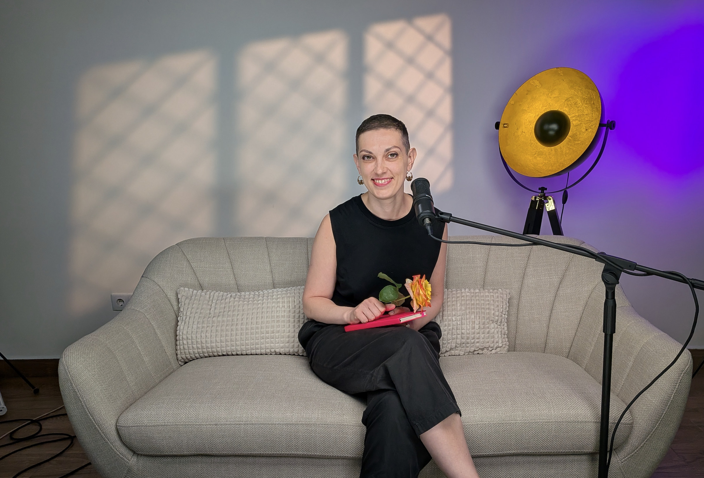Spark&Heal founder sitting and smiling on a sofa with a microphone and warm lighting